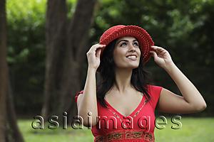 Asia Images Group - Half shot of woman wearing a red hat looking up, trees as background