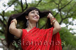 Asia Images Group - Indian woman wearing red sari smiling with hands in hair