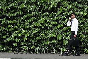 Asia Images Group - Indian man walking in front of green leafy hedge