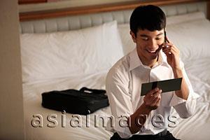 Asia Images Group - Young man looking at ticket and talking on phone smiling