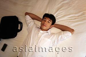 Asia Images Group - man laying on bed with hands behind his head.