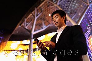 Asia Images Group - Young man in suit using phone in front of building at night