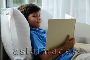 Asia Images Group - young boy sitting in bed reading book