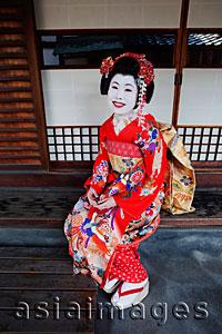 Asia Images Group - Geisha in red Kimono sitting in front of house