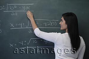 Asia Images Group - Rear view of young woman writing math equation on chalk board