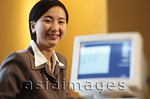 Asia Images Group - Female executive sitting at desk with computer, portrait, yellow background