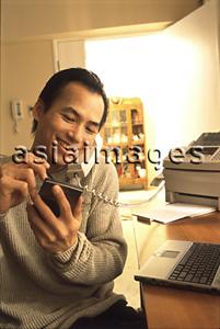 Asia Images Group - Man at home talking on telephone, holding palmtop