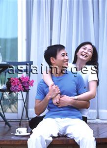 Asia Images Group - Couple sitting on balcony, embracing and laughing