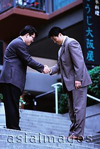 Asia Images Group - Two male executives bowing while shaking hands on stairway