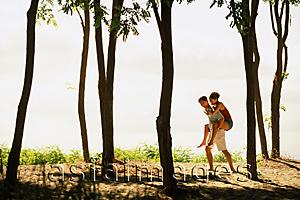 Asia Images Group - Man giving woman a piggyback ride amongst trees, by the beach