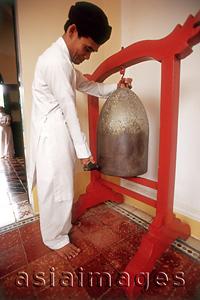 Asia Images Group - Vietnam, Tay Ninh, Cao Dai worshipper strike bell in Cao Dai Great Temple.