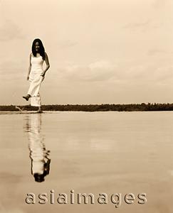 Asia Images Group - Reflection of woman in white dress kicking at water