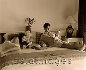 Asia Images Group - Woman and man in bed reading magazines, tray with cups on bed.