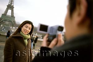 Asia Images Group - Man videotaping woman in front of Eiffel Tower, focus on woman.