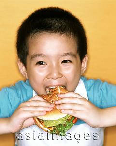 Asia Images Group - Young boy eating large hamburger, yellow background.