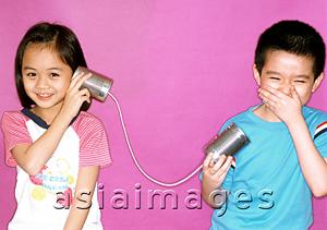 Asia Images Group - Children playing with toy string telephone, purple background.