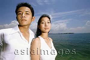 Asia Images Group - Young couple standing on beach, blue sky and beach in background, portrait