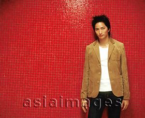 Asia Images Group - Young man in brown jacket leaning against orange/red background.