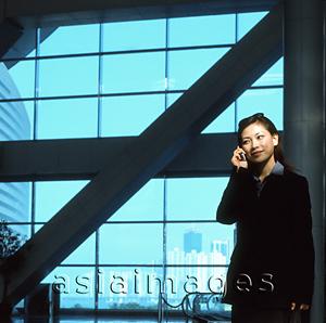Asia Images Group - Executive woman using cellular phone indoors, windows in background.