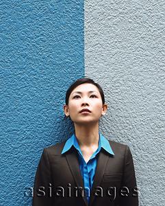 Asia Images Group - Executive woman standing against split colored background, looking up.
