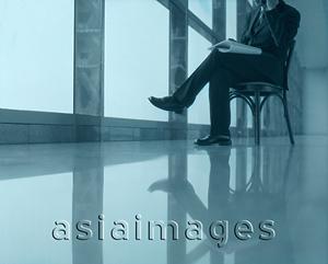 Asia Images Group - Executive sitting using cellular phone next to window, head not shown.