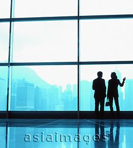 Asia Images Group - Silhouette of male and female executives by large window, skyline outside.