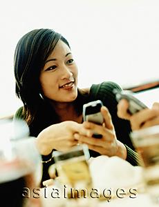 Asia Images Group - Young women holding cellular phone, looking off camera.