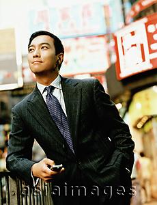 Asia Images Group - Executive holding cellular phone on street looking off camera.