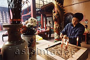 Asia Images Group - Malaysia, Kuala Lumpur, Chinatown, Man lighting joss sticks at Chinese temple.