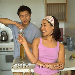 Asia Images Group - Couple in kitchen, man opening wine bottle, woman holding wine glass