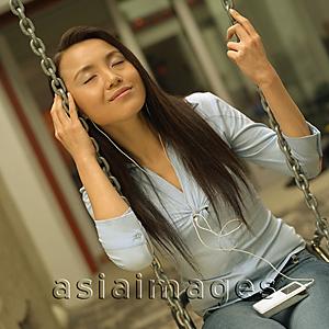 Asia Images Group - Young woman on swing, listening to personal stereo