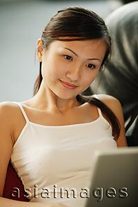 Asia Images Group - Young woman on sofa, using laptop, smiling