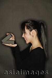 Asia Images Group - Young woman, side view, opening a box, black background