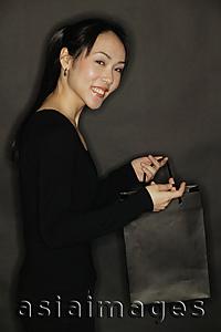 Asia Images Group - Young woman carrying shopping bag, black background