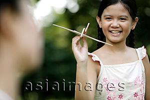 Asia Images Group - Young girl holding a paper airplane, mother in the foreground