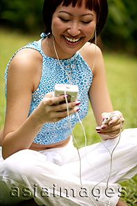 Asia Images Group - Young woman listening to personal stereo, looking down