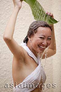 Asia Images Group - Young woman holding leaf, water cascading on her