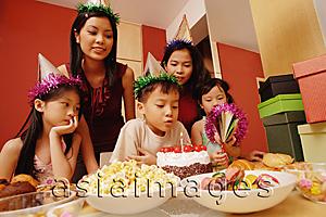 Asia Images Group - Young boy blowing out candles on a cake, surrounded by friends
