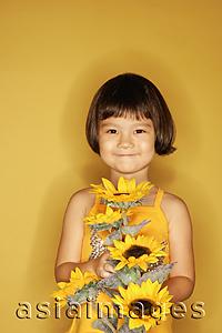 Asia Images Group - Young girl standing against yellow background, holding flowers, smiling