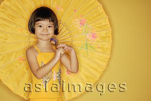 Asia Images Group - Young girl standing against yellow background, holding umbrella