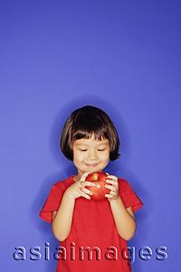 Asia Images Group - Young girl standing against blue background, holding an apple