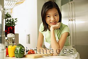 Asia Images Group - Young woman in kitchen, hand on chin, looking at camera
