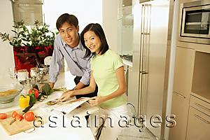 Asia Images Group - Couple in kitchen with cookbook, looking at camera