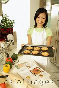 Asia Images Group - Young woman holding out baking tray, looking at camera