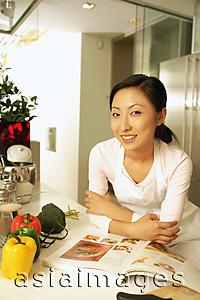 Asia Images Group - Young woman leaning on kitchen counter, looking at camera, smiling