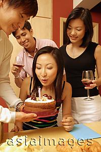 Asia Images Group - Woman blowing out candle on cake, surrounded by friends