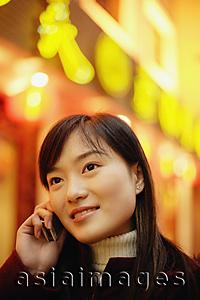 Asia Images Group - Young woman using mobile phone, neon signs behind her