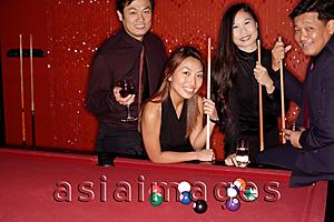 Asia Images Group - Men and women standing around pool table, looking at camera