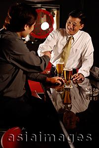 Asia Images Group - Two men shaking hands, beer glasses on table.