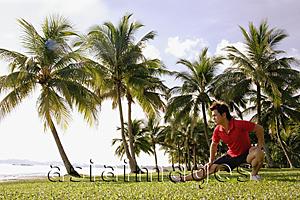 Asia Images Group -  Man doing stretching exercises in park, hand on knee